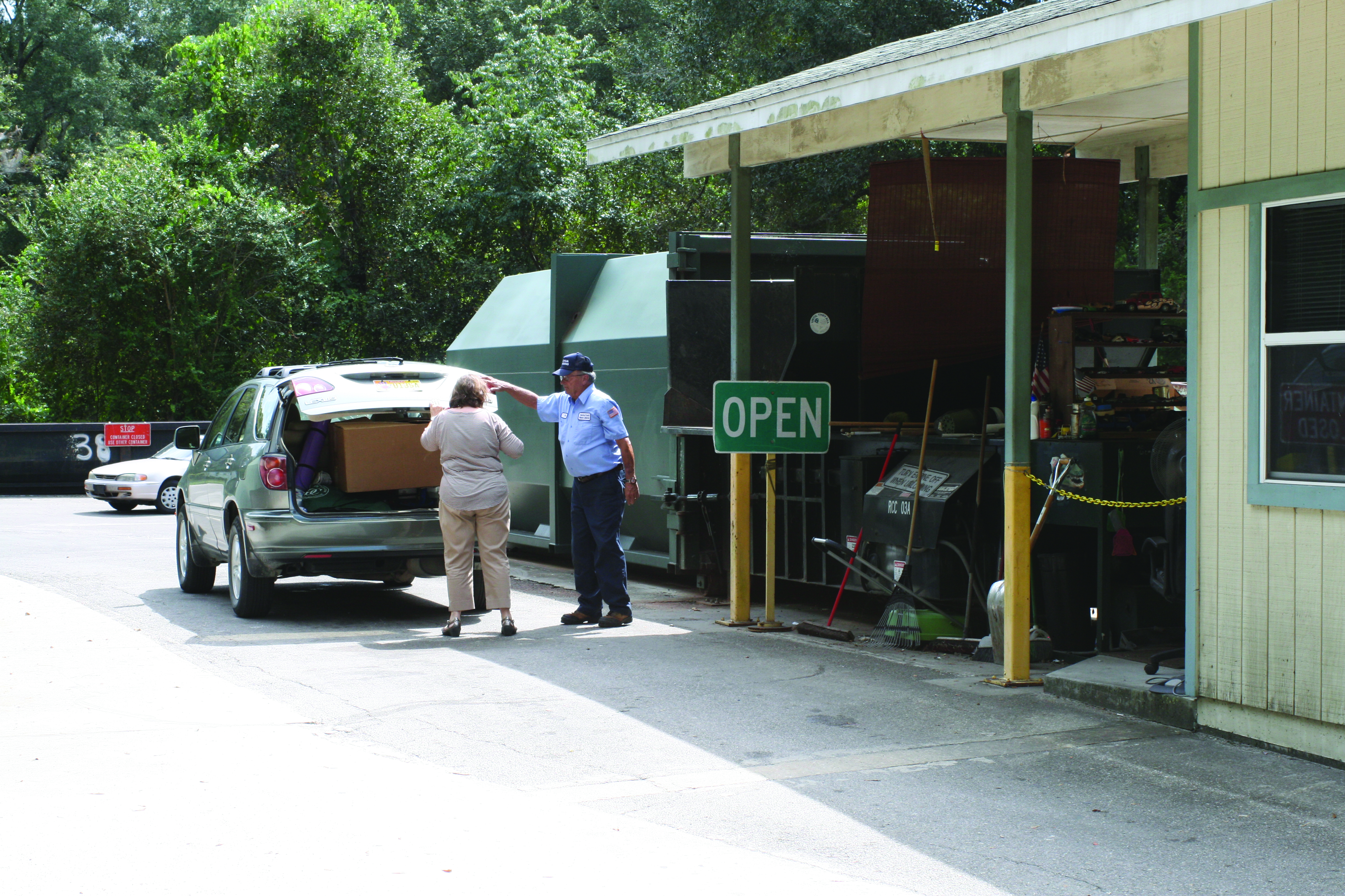 Image of Collection center attendant Helping customer alongside trash compactor.